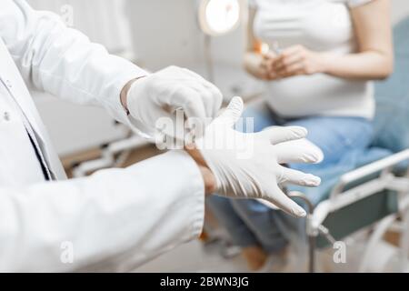 Doctor wearing medical gloves, preparing for medical examination procedure to a pregnant woman in the office Stock Photo