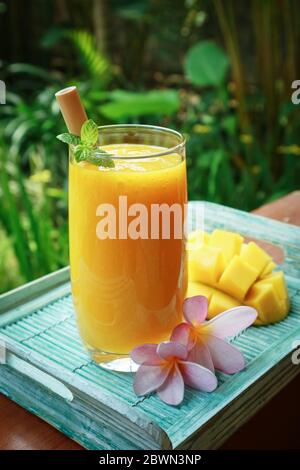 Mango smoothie in glass with bamboo drinking straws on wooden table outdoor, closeup Stock Photo