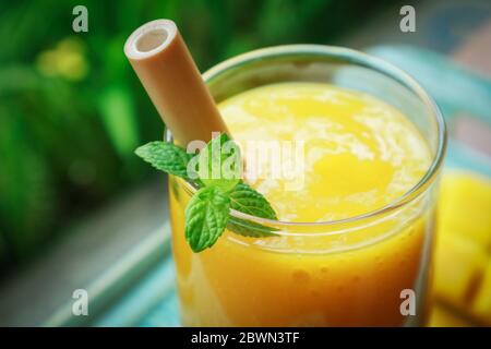 Mango smoothie in glass with bamboo drinking straws on wooden table outdoor, closeup Stock Photo