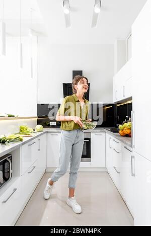 Woman cooking healthy food on the modern kitchen at home, wide interior view. Woman is motion blurred Stock Photo