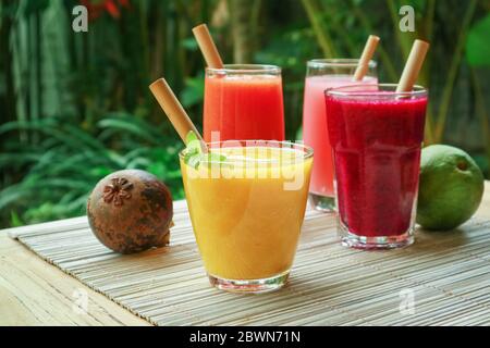 Dragon fruit, papaya and mango smoothies in glasses with bamboo drinking straws and fresh tropical fruits  outdoor Stock Photo