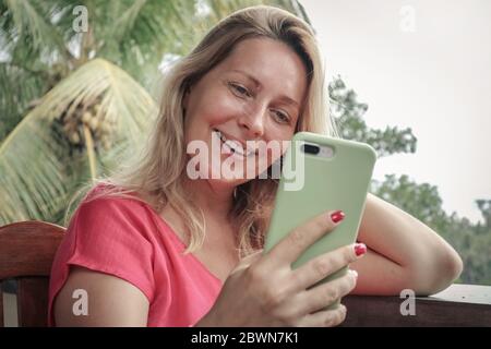Adult blond woman using  smart phone for video call outdoor on Bali island, Indonesia. Stock Photo