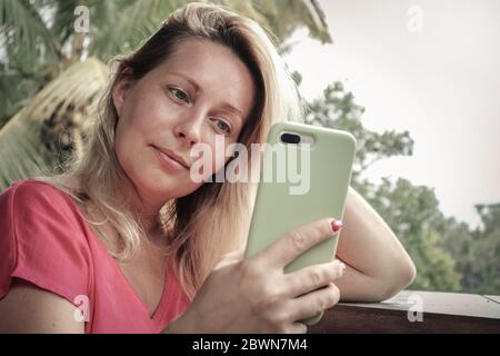 Adult blond woman holding , using and looking at smart phone outdoor Stock Photo