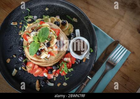 Pancakes with banana, blueberries, strawberries and chocolate sauce on a plate top view Stock Photo