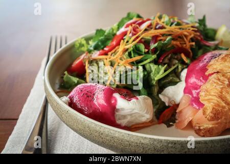 Smoked salmon , hash brown potato, semi sundried cherry tomato, beet sauce, poached eggs, on warm butter croissant, chives, mixed herbs, crush pistach Stock Photo