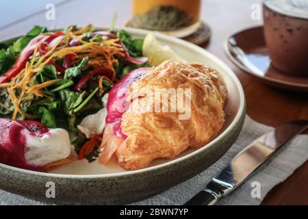 Smoked salmon , hash brown potato, semi sundried cherry tomato, beet sauce, poached eggs, on warm butter croissant, chives, mixed herbs, crush pistach Stock Photo