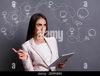 Creative business lady with digital tablet and light bulbs above full of ideas, innovation, business idea concept, grey background Stock Photo