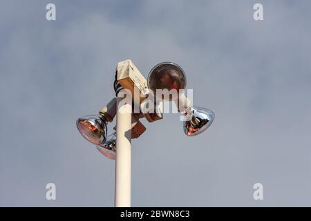 Outdoor security spotlights stand tall and are photographed from below against a cloudy sky. Stock Photo