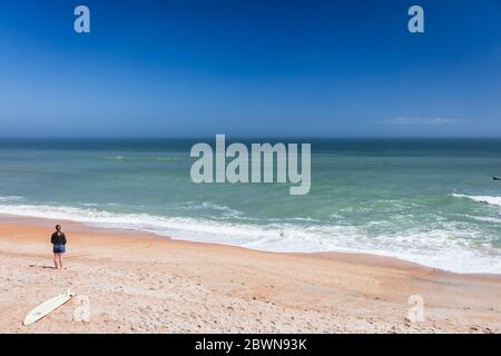 Woman stand alone on empty Florida beach with surfboard Stock Photo