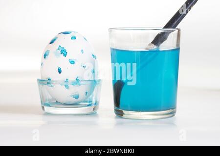 Easter egg painted with blue dots and a glass with a brush and blue colored water forhomemade holiday decoration, gray background with copy space, sel Stock Photo