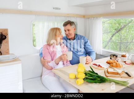 Affectionate mature couple having breakfast together inside of their camper van during vacation Stock Photo