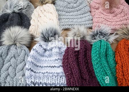 selection of hand crafted hats by knit or crochet with fake fur pom poms on a table for sale at a craft fair Stock Photo