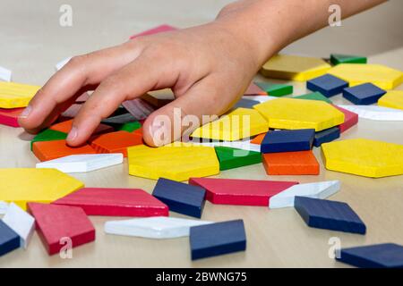 Bright colored tangram child geometric shape puzzle pieces  in a pile close up with hand moving pieces. Stock Photo