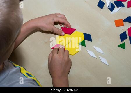 Tangram geometric colored shapes puzzle piece looking over child's shoulder to pieces on brown table. Education and problem solving concept. Stock Photo