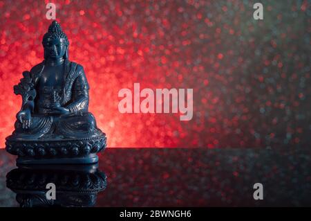Blue Medicine Buddha on a red and black gradient background with stars and reflection Stock Photo