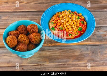 Falafel balls in a dish and hummus, chickpea, tahini with olive oil, pepper, spices in a plate on wooden table. Traditional Middle Eastern healthy vegan food. Stock Photo