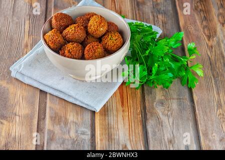 Falafel balls in ceramic plate and green fresh parsley on a wooden background.Falafel is a traditional Middle Eastern food, commonly served in a pita. Stock Photo