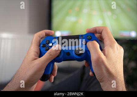 man hands holding joystick and playing video game at home on coach sofa in front of television with play game concole Stock Photo