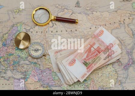 A compass with a bundle of big money and a magnifying glass are on the map Stock Photo