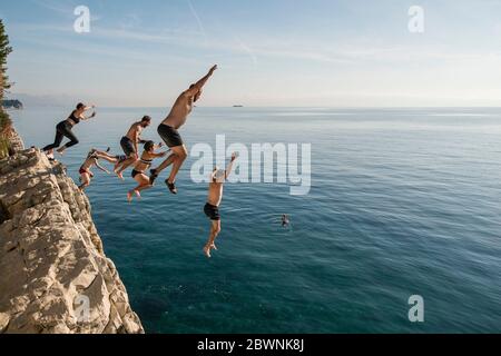 Friends jumping off cliff into Adriatic Sea near Split, Croatia Stock Photo