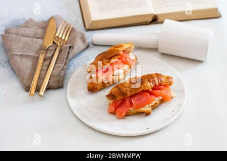 Breakfast with croissant, cream cheese and smoked salmon. Old rustic book on the background. Stock Photo