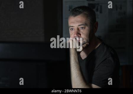 Man works on a computer at night. Attractive man sitting at desk table looking at laptop computer in dark room late at night. Stock Photo