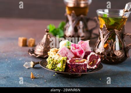 Bowl with various pieces of turkish delight lokum and black tea with mint on a dark background Stock Photo