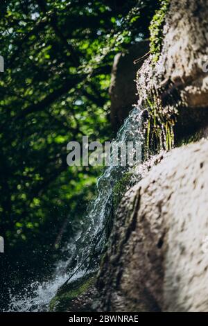 Water splashes on a large stone. Splashes of a small waterfall in the grotto. Park with a natural waterfall Stock Photo