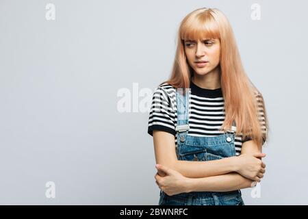 Studio portrait of displeased/angry cute blonde woman in striped t-shirt frowning her face in displeasure and keeping arms folded, looking away. Close Stock Photo