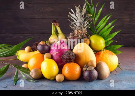 Assortment of exotic fruits with palm leaves on dark background Stock Photo