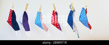 Several homemade community face masks from colorful cotton against coronavirus pandemic hanging on a clothesline, gray background, panoramic format, s Stock Photo