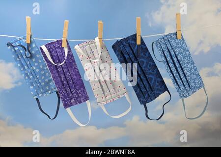 Homemade community face masks from cloth as protection against coronavirus pandemic are hanging on a clothesline, blue sky with clouds Stock Photo