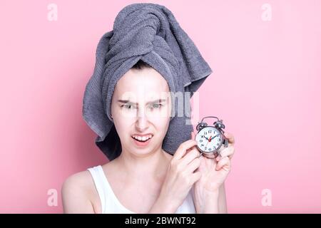 Dissatisfied young girl shows on alarm clock, overslept on pink background Stock Photo