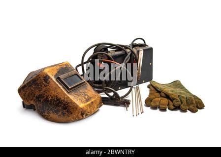 Aged welding mask with welding machine, protective gloves, and arc steel electrodes isolated on white background. Kit of welder time-tested. Stock Photo