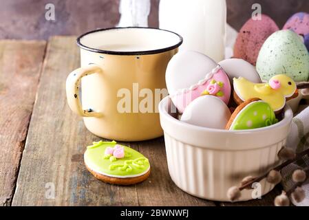 Eggs shaped Easter cookies, hand-made with cup of milk. Decorated with fondant icing on old wooden background Stock Photo