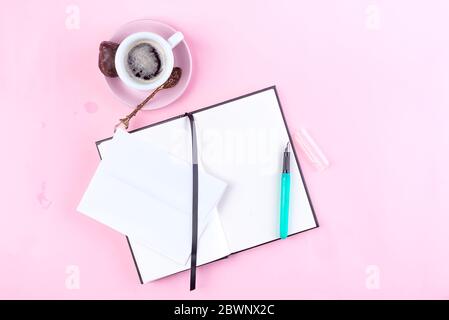 Morning coffee mug for breakfast, empty notebook, pencil and envelope on pink table top view . Woman working desk. Stock Photo