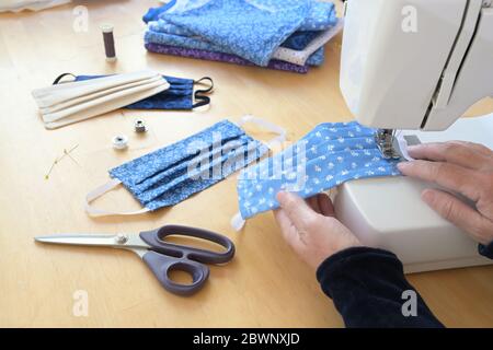 Hands of an older woman on a sewing machine making community face masks during the coronavirus pandemic, homemade protection against infection, select Stock Photo
