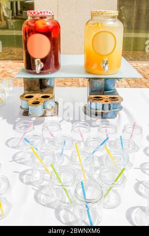 Set of glass jars with plastic straws on a table next to some jars of sweet peach juice and lemonade. Stock Photo