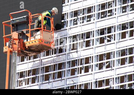 Belgrade, Serbia - May 6, 2020: Construction worker in crane basket installing sheets cladding for covering metal structure on a building facade wall Stock Photo