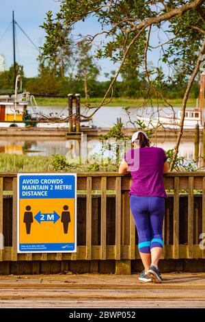 Female jogger resting on the Steveston waterfront after while maintaining space from others during Covid 19 Stock Photo