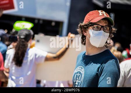 05-30-2020 Tulsa USA - Man in classes and cap and Legal Aid Bureau tee-shirt glances backward with blurred protesters at BLM rally behind him Stock Photo