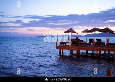 Dawn of the sun rising from the horizon of the sea. Pontoon moored on the seashore with sunbeds and umbrellas Stock Photo