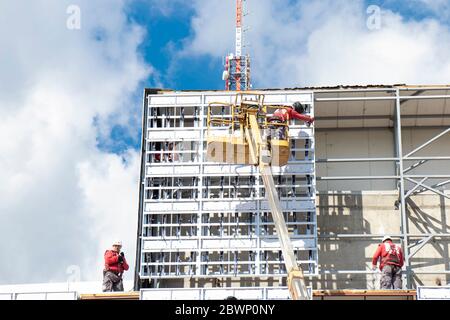 Belgrade, Serbia - May 6, 2020: Construction workers on construction site making external cladding structure on a building facade wall with crane Stock Photo