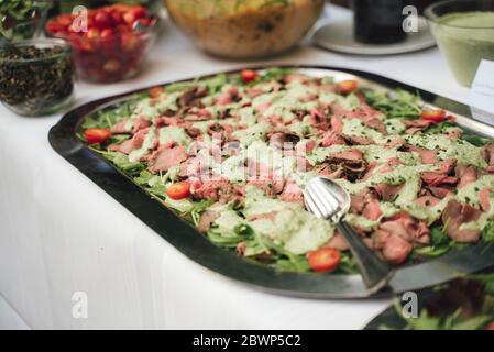 Stainless tray with slices of roast beef poured with green cream sauce. Self-service buffet table. Celebration, party, birthday or wedding concept. Stock Photo