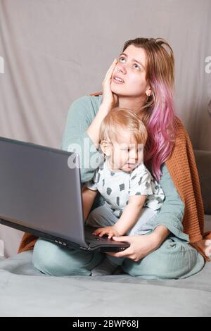Stay at home, mom works remotely on a laptop, taking care of her child. A young mother on maternity leave is trying to work as a freelancer with a bab Stock Photo