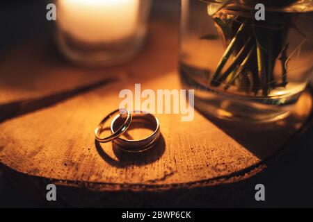 Pair of marriage rings laying on wooden surface. Warm tones by candle light. Orange toned. Stock Photo