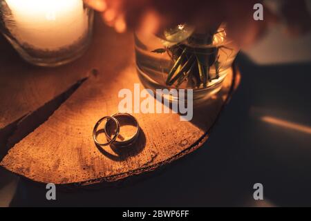 Top view of wedding rings couple laying on wooden slice of tree trunk in candle light. Warm orange toned colors. Stock Photo