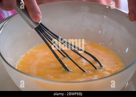 Beating eggs with a whisk. Bowl with beaten eggs Stock Photo