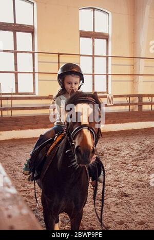 Cute small kid girl learning to ride a horse in farm corral. Portrait Stock Photo