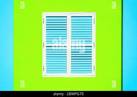Traditional vintage Singapore shop house window with antique blue and white wooden shutters on green and blue wall in historic Little India Stock Photo